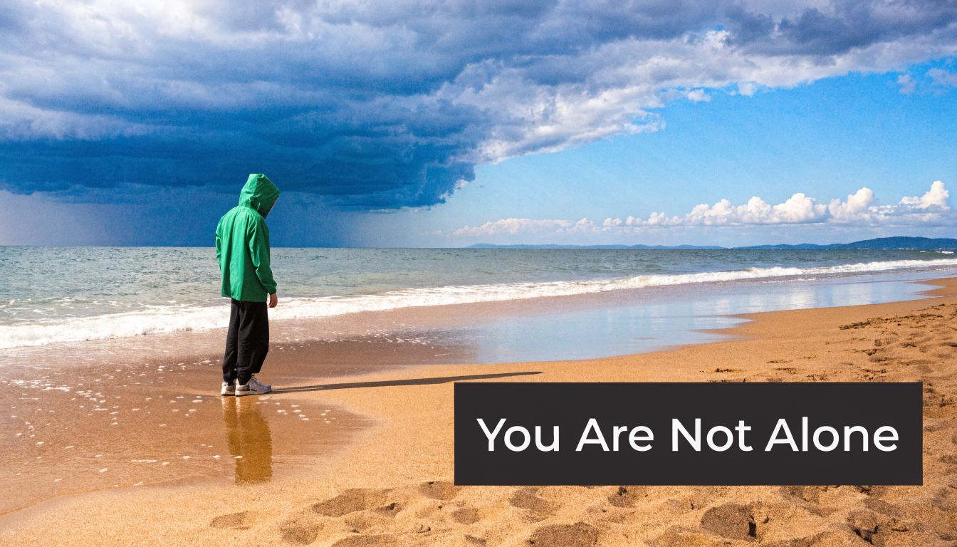 A person in a green hooded jacket standing alone on a sandy beach under dark stormy clouds.