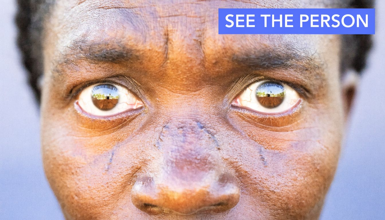 Close-up of a person's eyes reflecting a scene, with the text SEE THE PERSON overlayed.